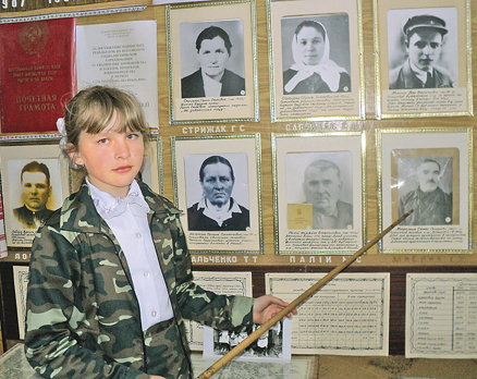 Юний екскурсовод Юлія Стрижак розповідає про голів колгоспу, які рятували  односельців від голоду. Крайній праворуч у верхньому ряду портретів — Іван Мисник,  крайній праворуч у нижньому ряду — Семен Москаленко. Фото автора
